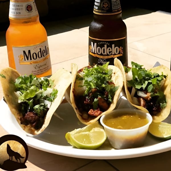 Three Mexican tacos with cilantro and onions, salsa, lime, and two Modelo beers.