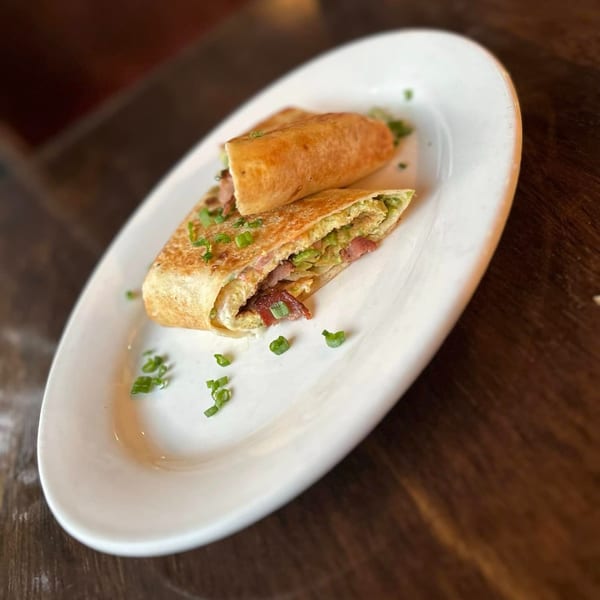 Two Mexican breakfast burritos, one cut open to show eggs, bacon, and green onions, on a white plate.