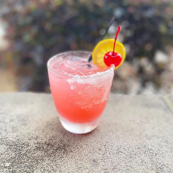 Pink margarita with a salted rim, garnished with a lemon slice and a cherry.