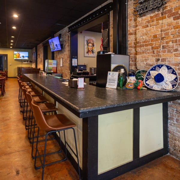 Interior of Coyoacan Mexican Restaurant, showing a long bar with stools, brick walls, and Mexican decor.