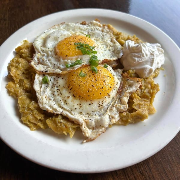 Two fried eggs with green onions and black pepper on a bed of chilaquiles with a dollop of sour cream.