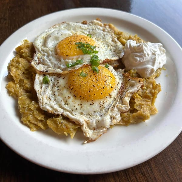 Two fried eggs with green onions and pepper, served over chilaquiles with a side of sour cream.