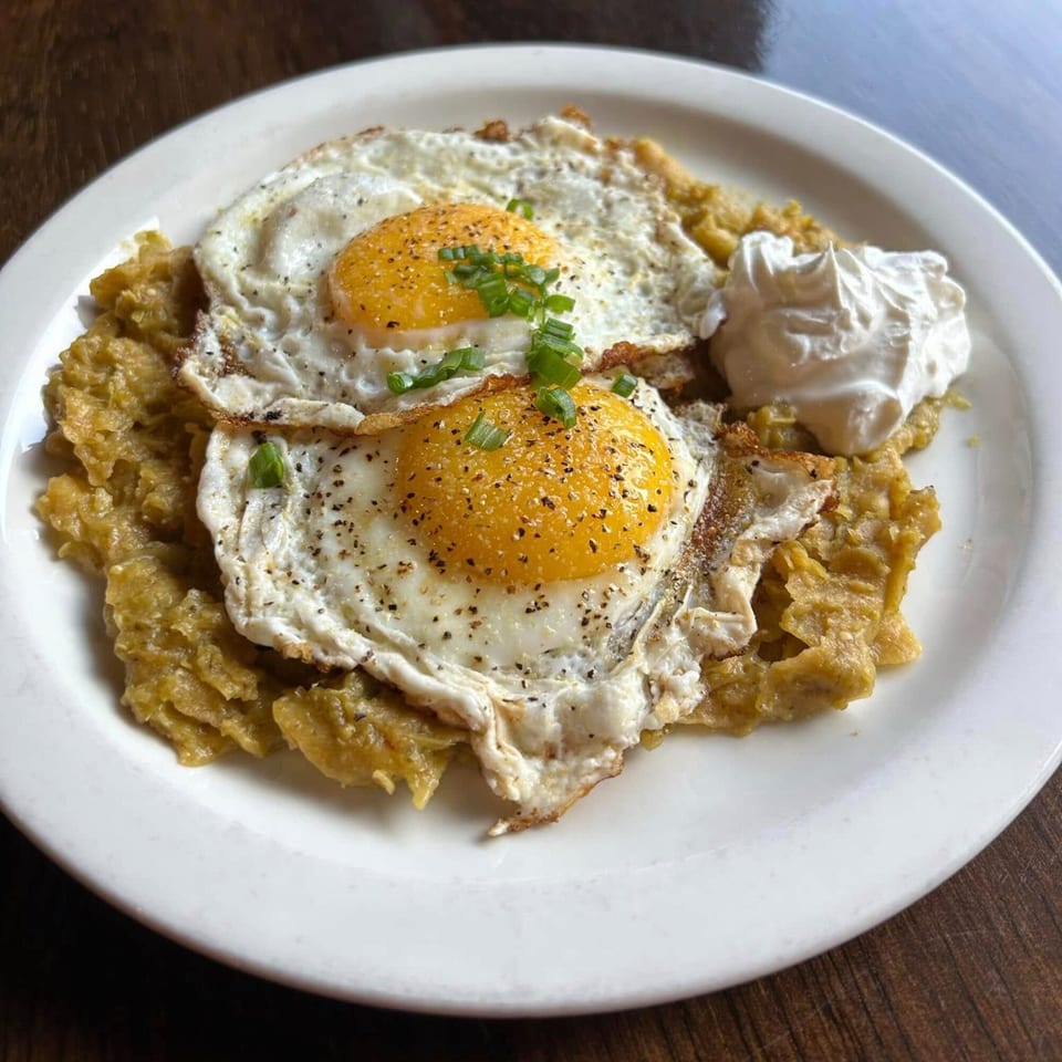 Two fried eggs with green onions and pepper, served over chilaquiles with a side of sour cream.
