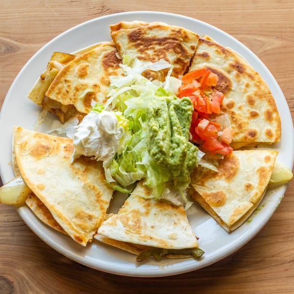 A plate of Coyoacan Mexican Restaurant's quesadillas with guacamole, sour cream, lettuce, and diced tomatoes.