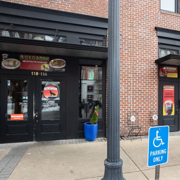 Exterior of Coyoacan Mexican Restaurant with brick facade, black doors, and a blue accessible parking sign.