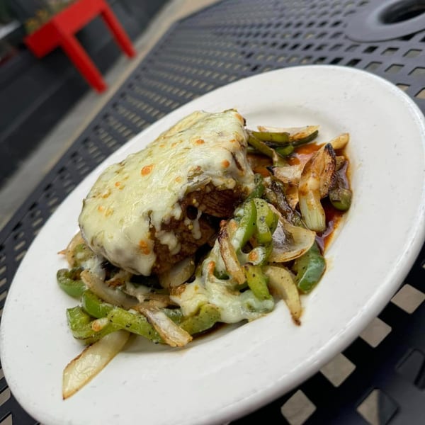 Mexican dish with melted cheese over meat, green peppers, and onions on a white plate.