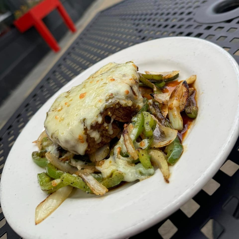 Mexican dish with melted cheese over meat, green peppers, and onions on a white plate.