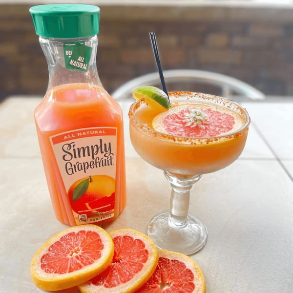 A grapefruit margarita with a lime and grapefruit slice, next to a bottle of grapefruit juice.
