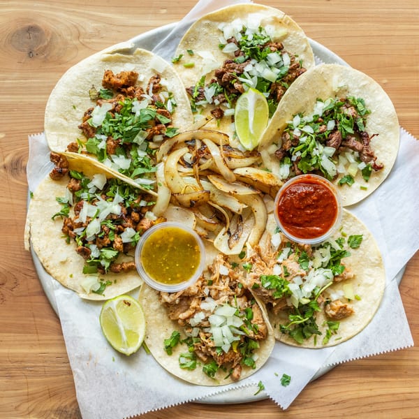 A platter of Coyoacan Mexican Restaurant tacos with various meats, onions, cilantro, limes, and salsas.