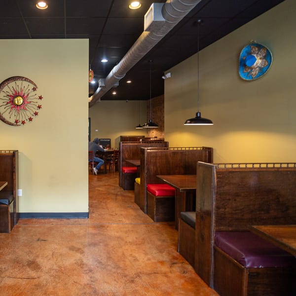 Interior of Coyoacan Mexican Restaurant with empty wooden booths, a concrete floor, and decorative wall art.