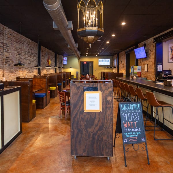 Interior of Coyoacan Mexican Restaurant with booths, a bar, and a "Please Wait to be Seated" sign.