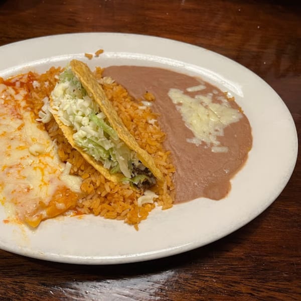 A Mexican combination plate with a taco, enchilada, rice, and refried beans on a white plate.