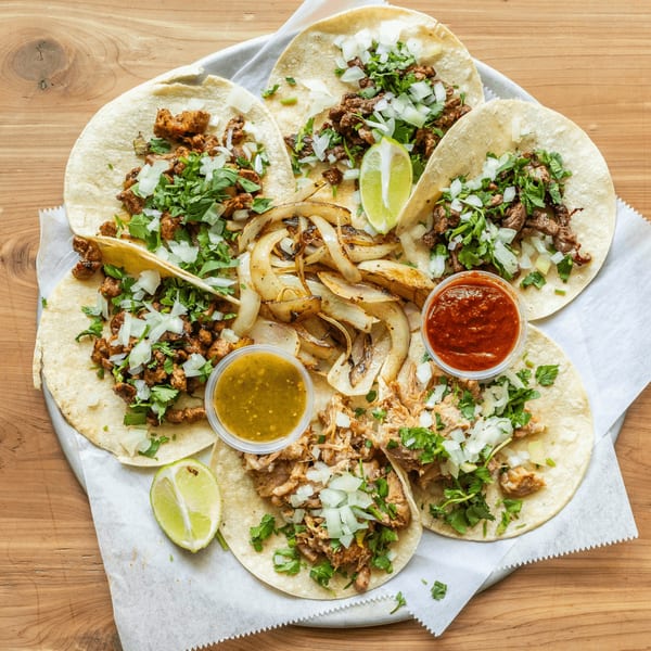A platter of Coyoacan Mexican Restaurant tacos with various meats, onions, cilantro, limes, and salsas.