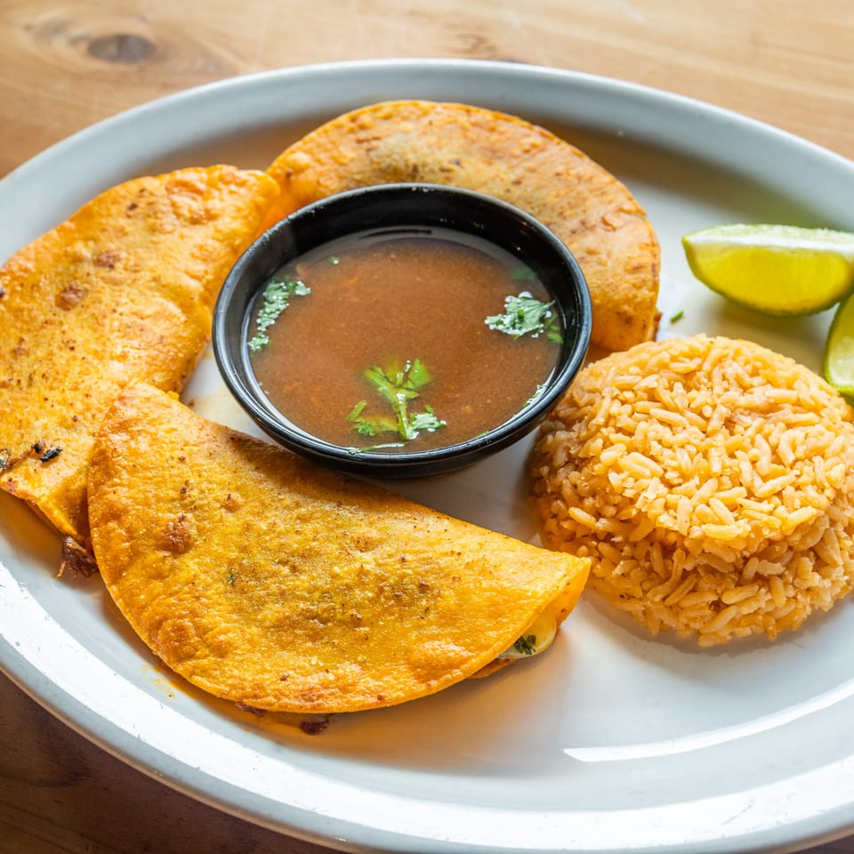 Three golden-fried quesadillas, a bowl of consommé, and a mound of Mexican rice with lime wedges.