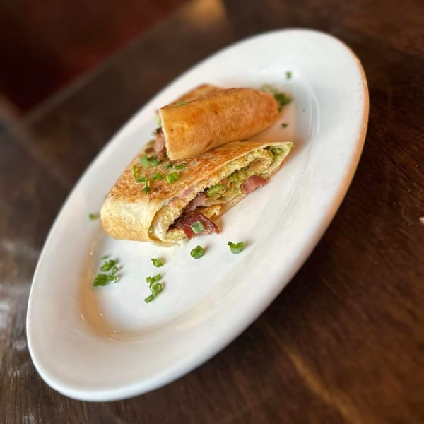 Two Mexican burritos, one sliced open to show bacon, egg, and green onions, on a white plate.