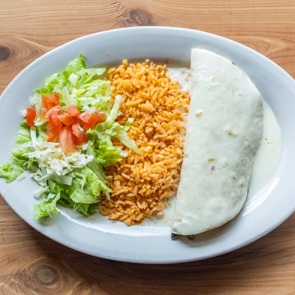 A Mexican burrito covered in white sauce, with a side of rice, lettuce, and diced tomatoes.