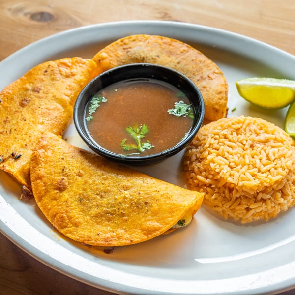 Three golden-fried quesadillas with a side of rice, lime wedges, and a bowl of consommé.