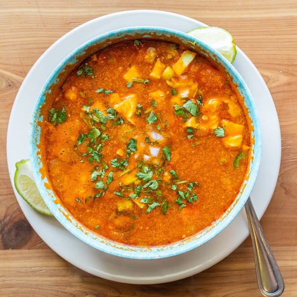 Overhead view of a vibrant orange Mexican soup with cilantro and diced vegetables in a blue bowl.