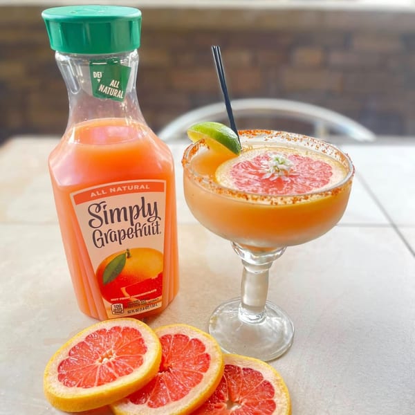 Grapefruit margarita with a lime wedge and a bottle of Simply Grapefruit juice on a table.