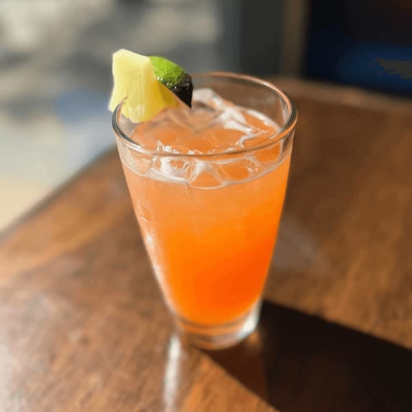 A vibrant orange cocktail with ice, garnished with a pineapple wedge and lime, on a wooden table.