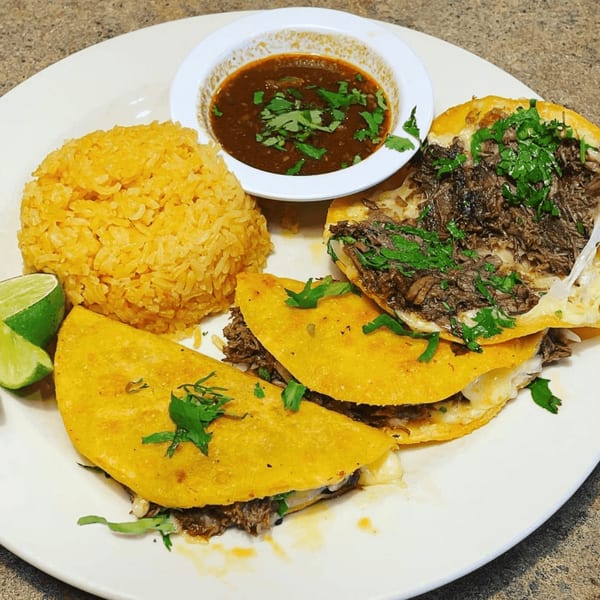 Three birria tacos with rice, lime wedges, and a side of consommé on a white plate.