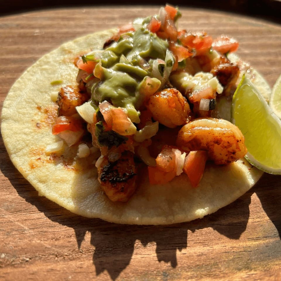A Coyoacan Mexican Restaurant shrimp taco with guacamole, pico de gallo, and a lime wedge.