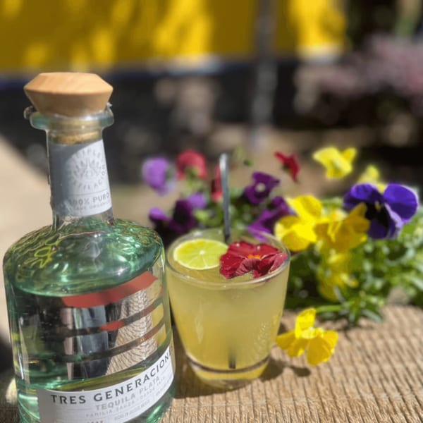 A bottle of Tres Generaciones tequila next to a margarita garnished with lime and flowers.